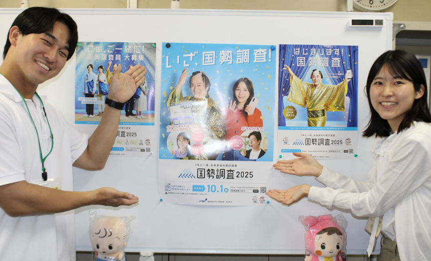 国勢調査のポスターの前で立つ新規採用職員と指導担当者