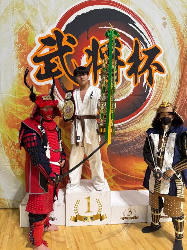 表彰台でトロフィーとベルトを持つ田中さん